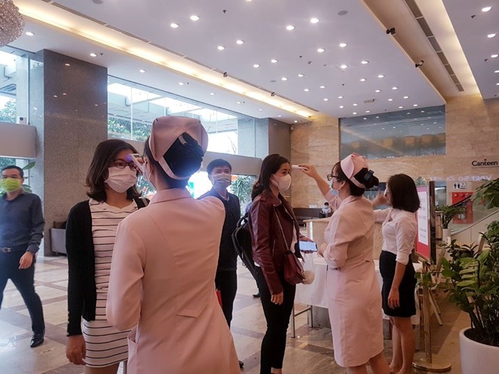 Nhân viên y tế PKĐK Hoàng Long đang đo thân nhiệt cho mọi người ra vào tòa nhà VCCI