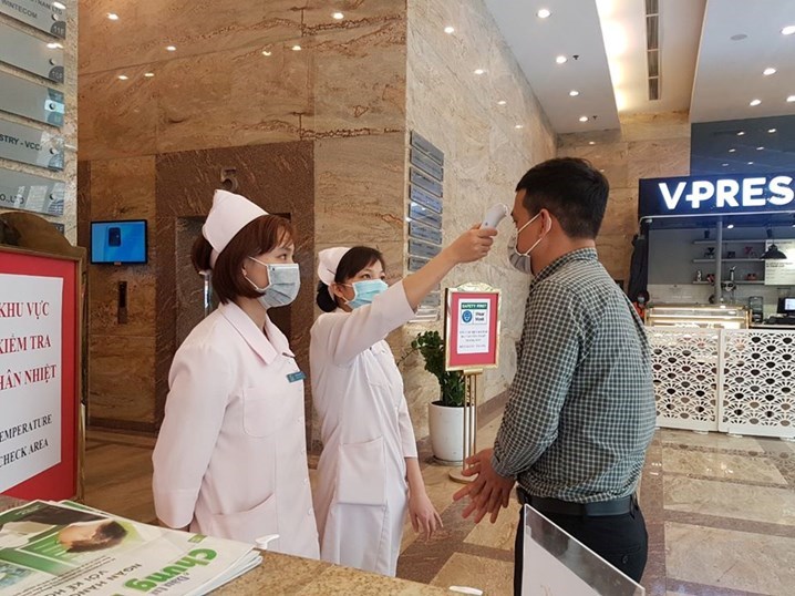 Nhân viên y tế PKĐK Hoàng Long kiểm tra thân nhiệt cho KH trước khi vào phòng khám